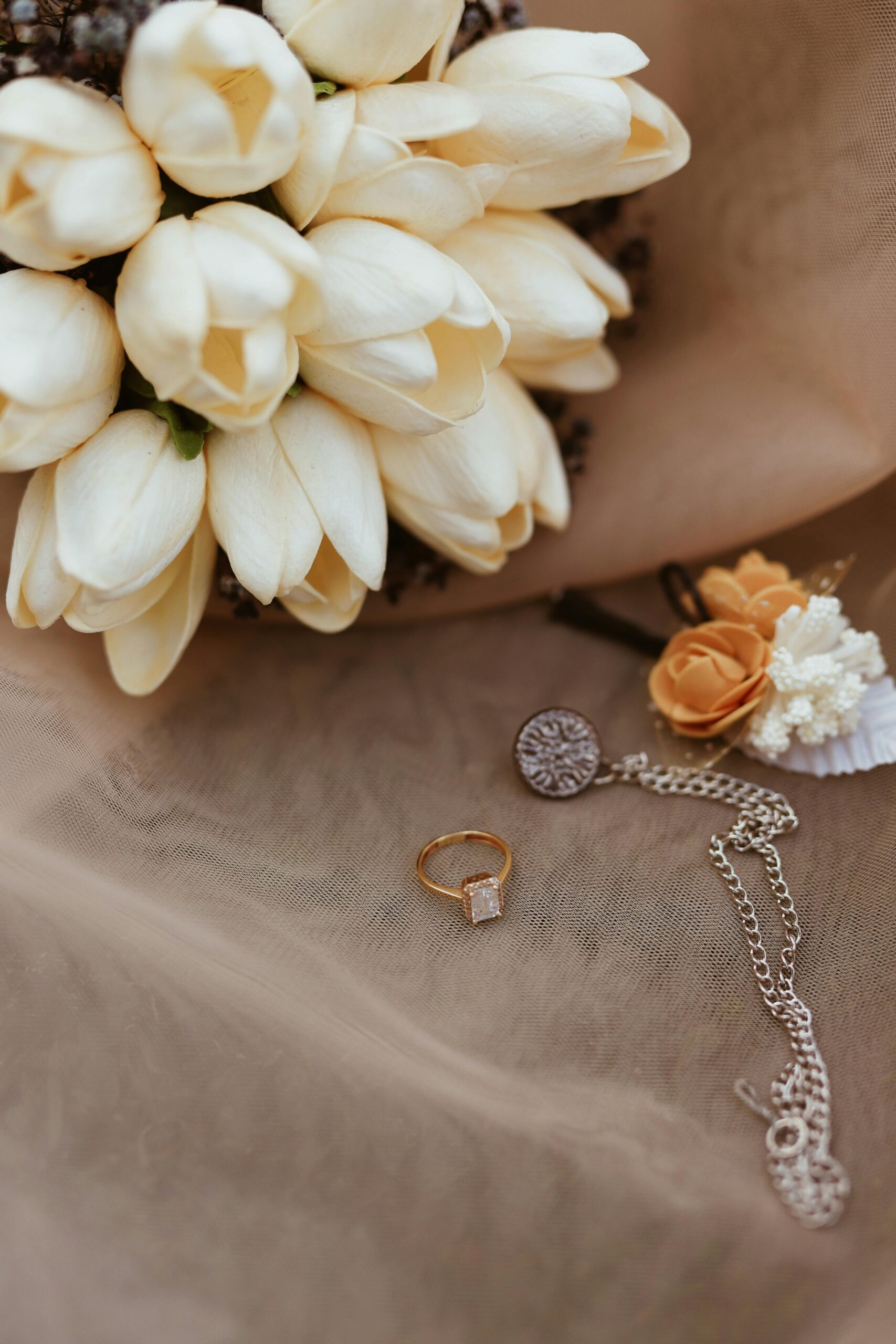 A collection of wedding accessories including an ivory bouquet and jewelry on a soft fabric.