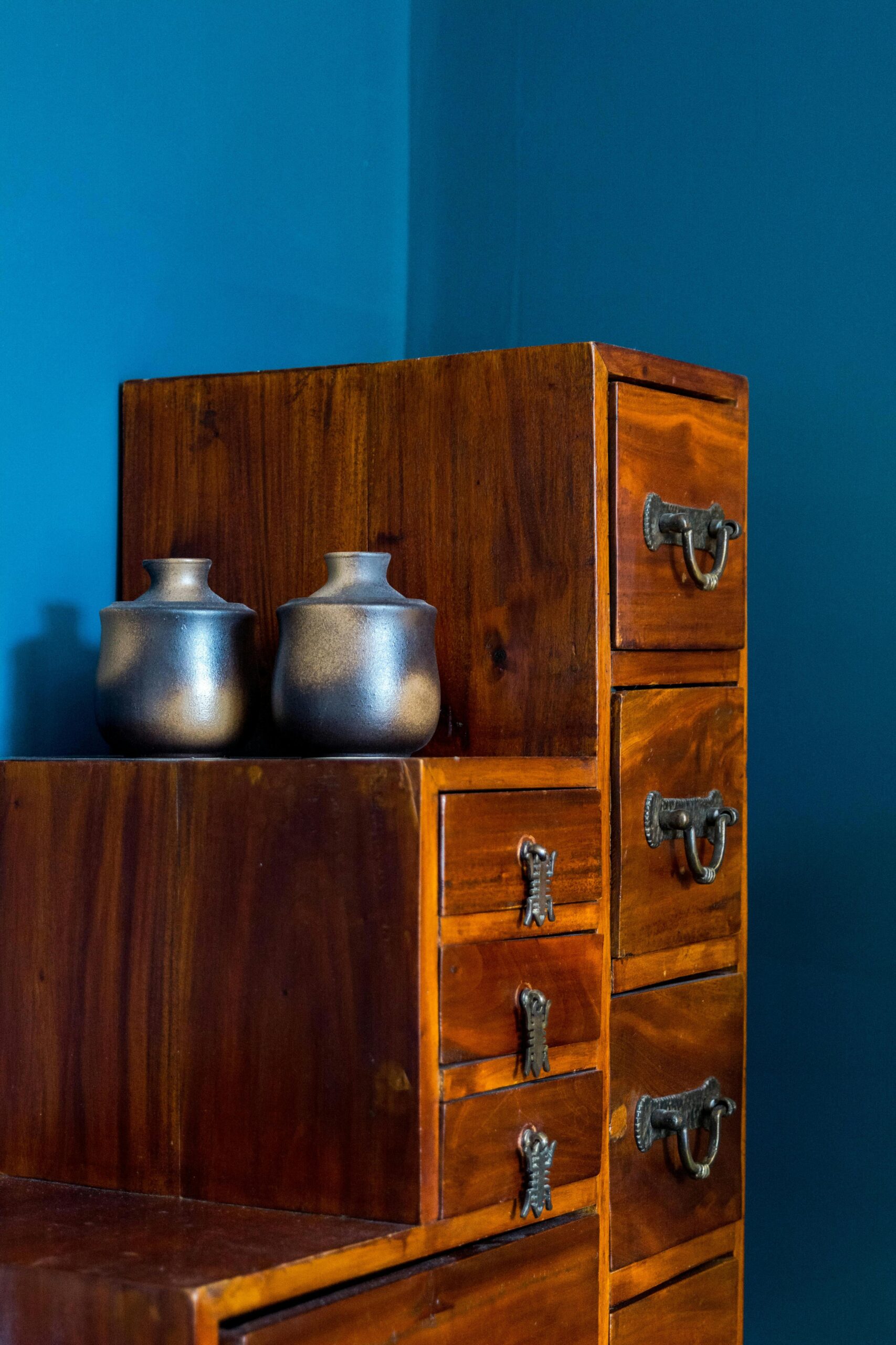 Elegant wooden cabinet against blue wall with metal vases, creating a cozy interior setting.