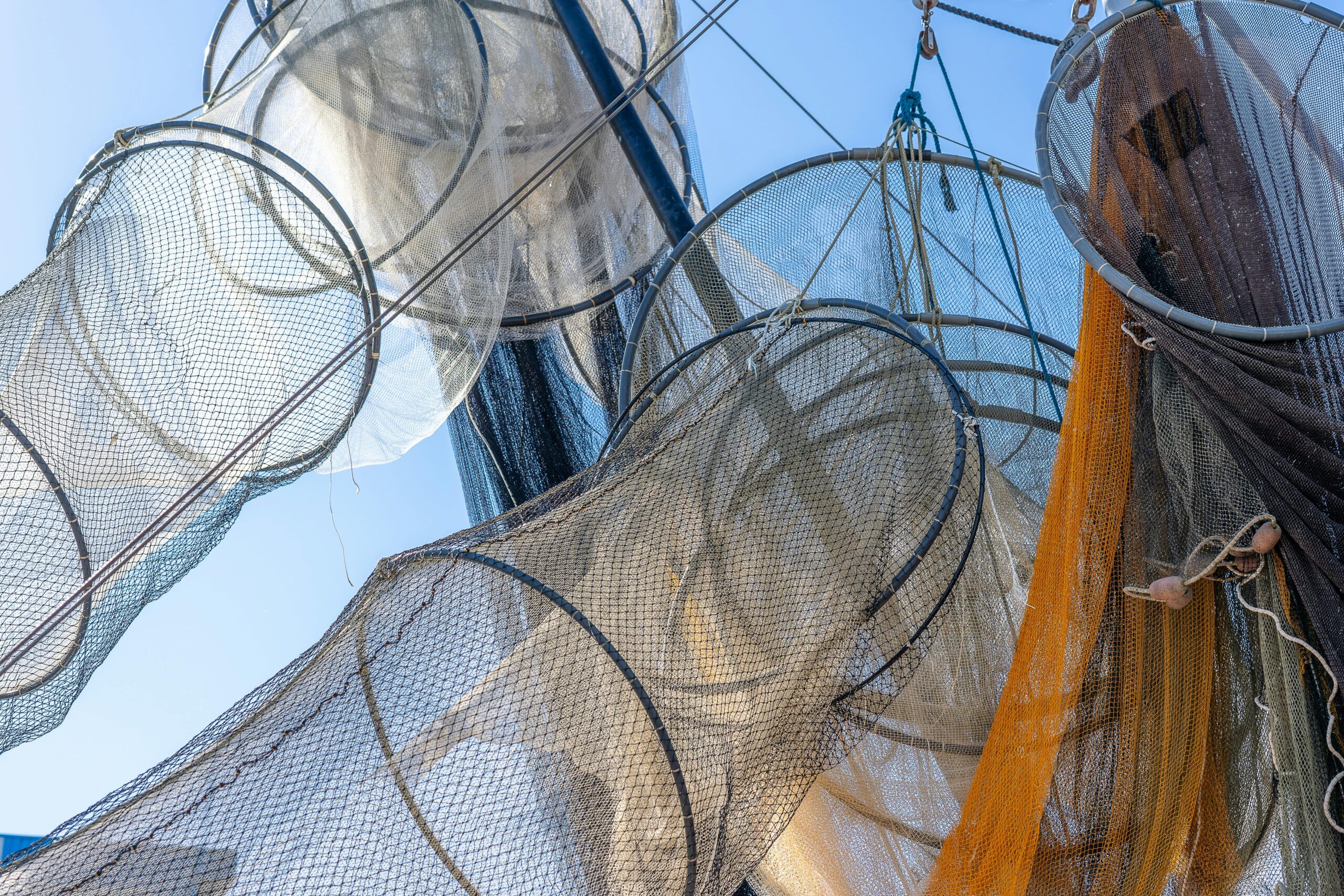 A low angle view of various fishing nets hanging under a blue sky, showcasing patterns and textures.