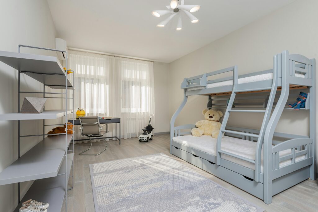A bright and spacious children's bedroom with contemporary bunk beds, desk, and toys.
