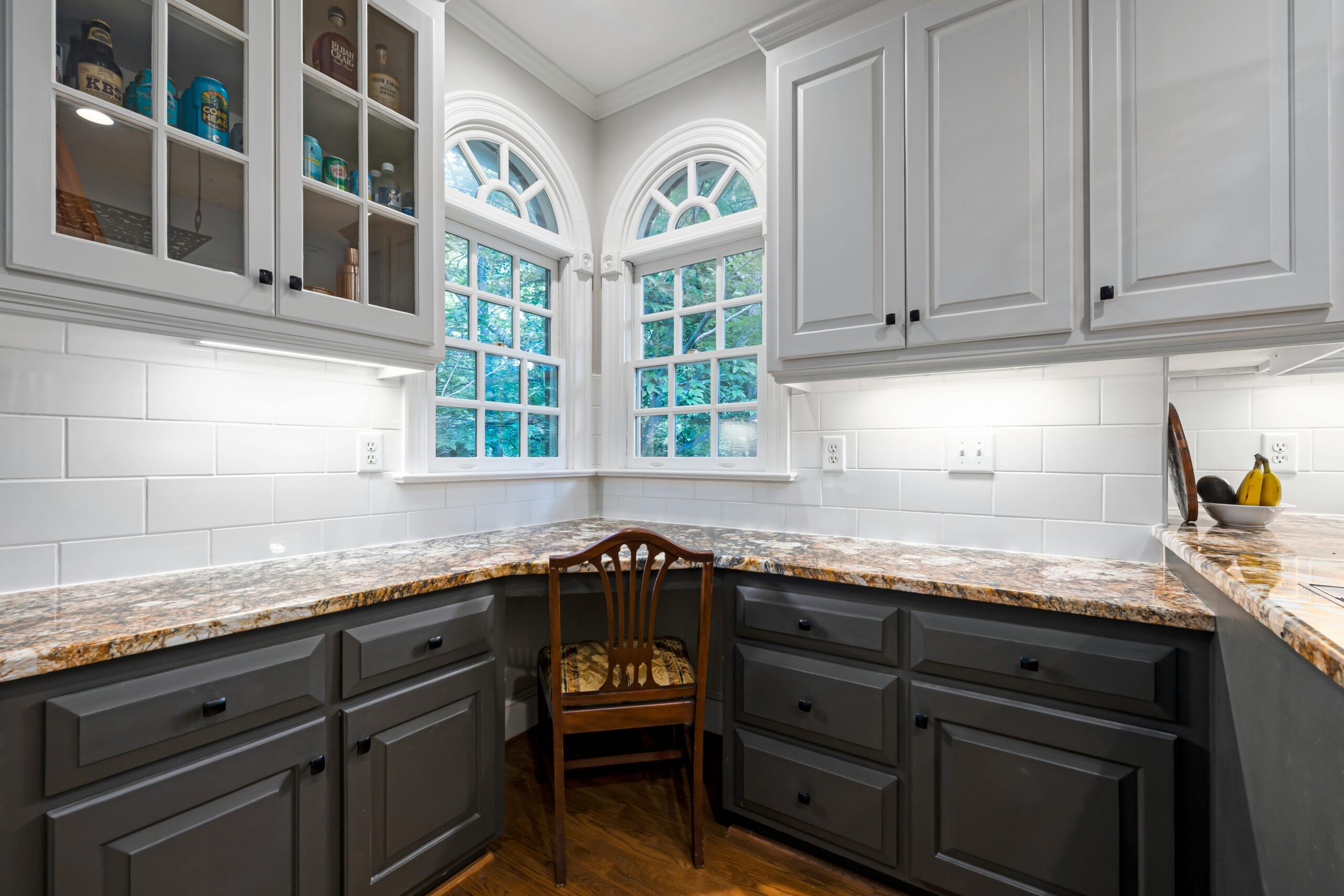 Modern kitchen interior featuring granite countertops, white cabinets, and arched windows.