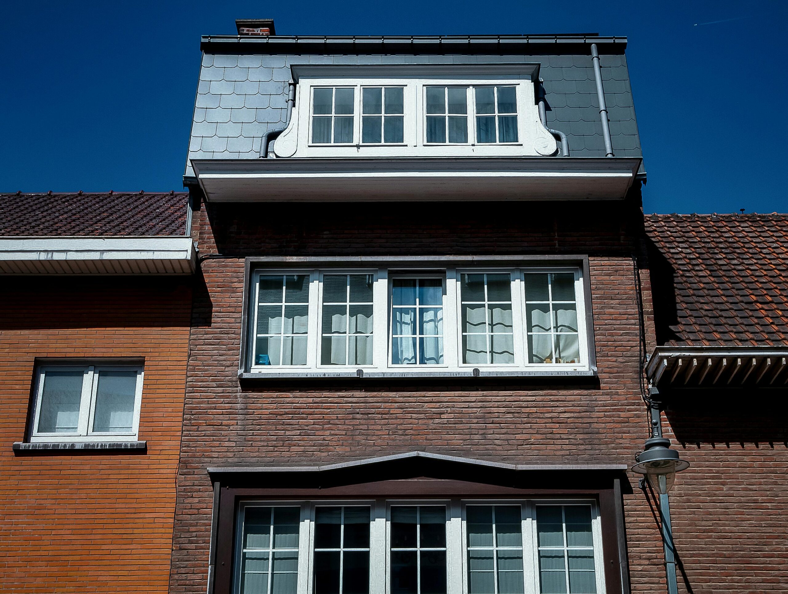 Close-up view of a traditional brick house facade with dormer windows under a clear blue sky.