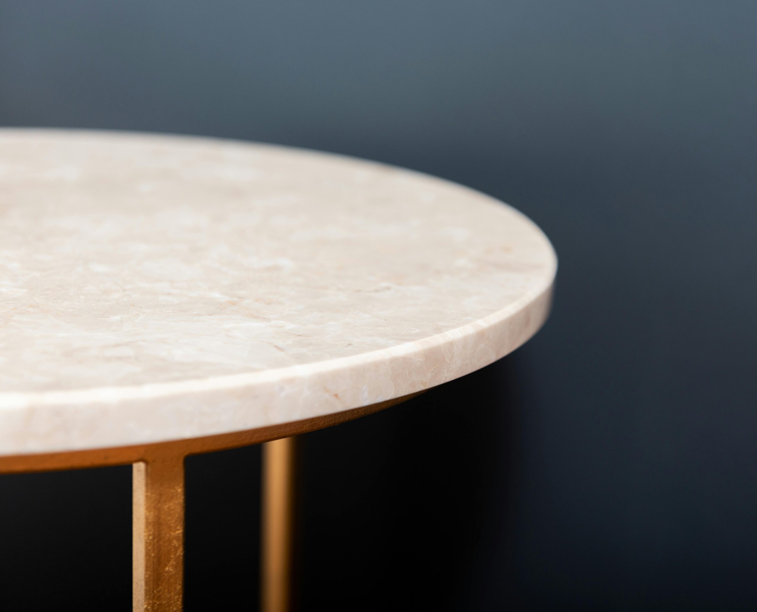 Close-up of a marble top round side table with gold legs against a dark background.