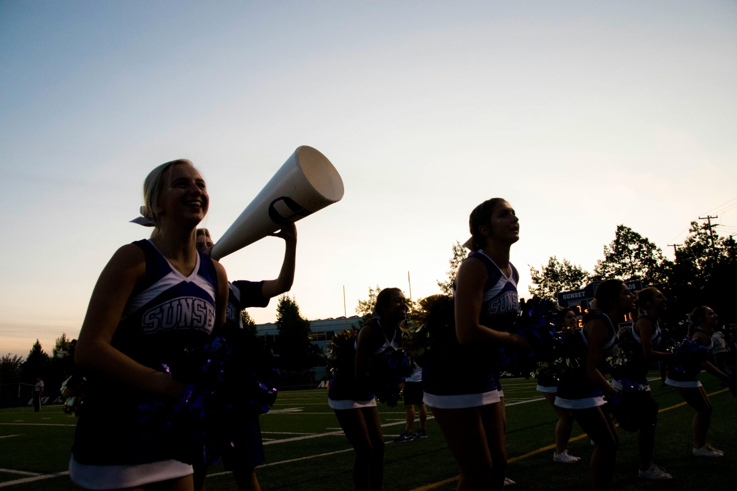 Group of cheerleaders performing on a field during sunset, adding energy to a sports event.