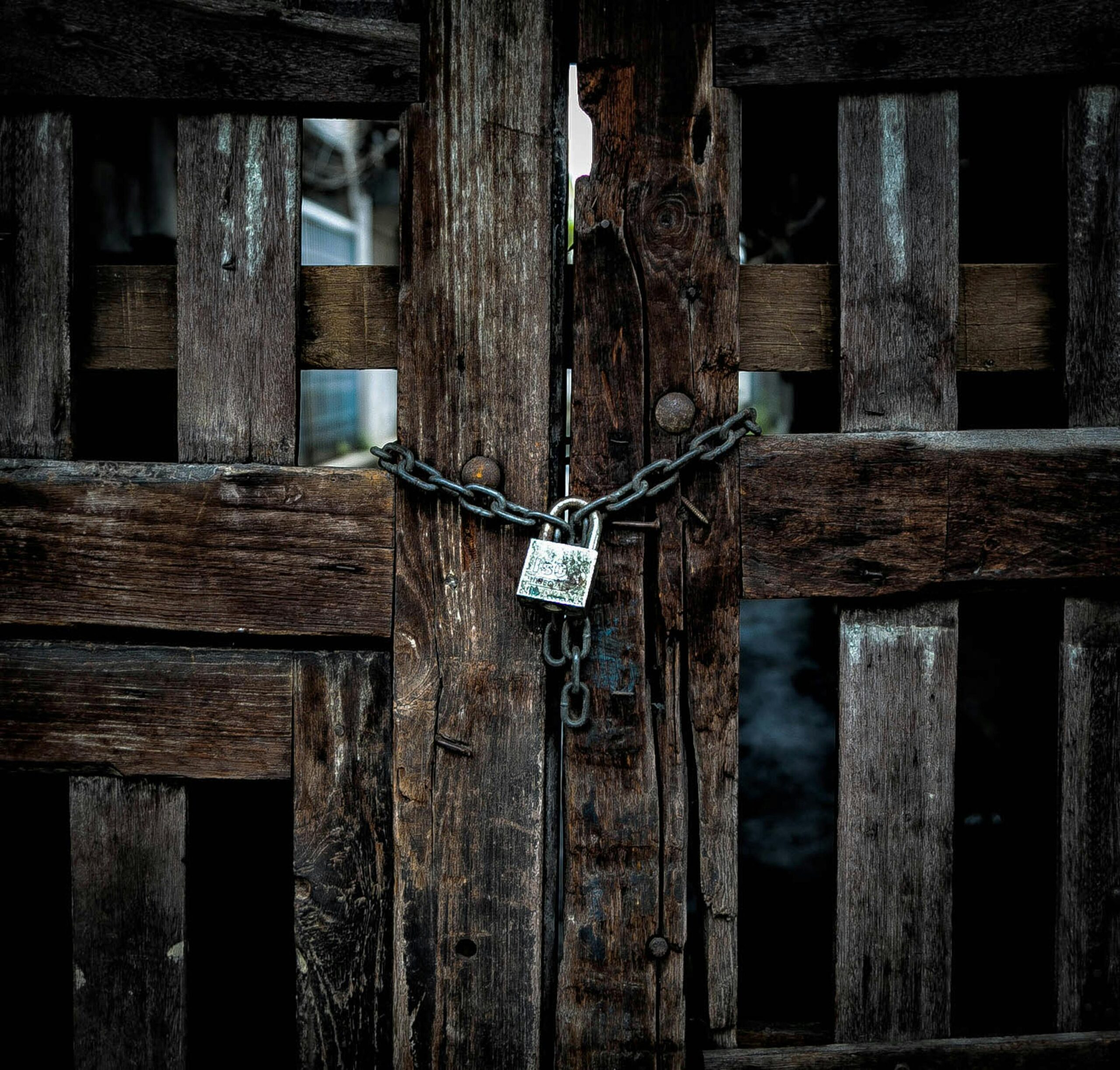 Close-up of a locked rustic wooden gate with a chain and padlock, symbolizing security and protection.