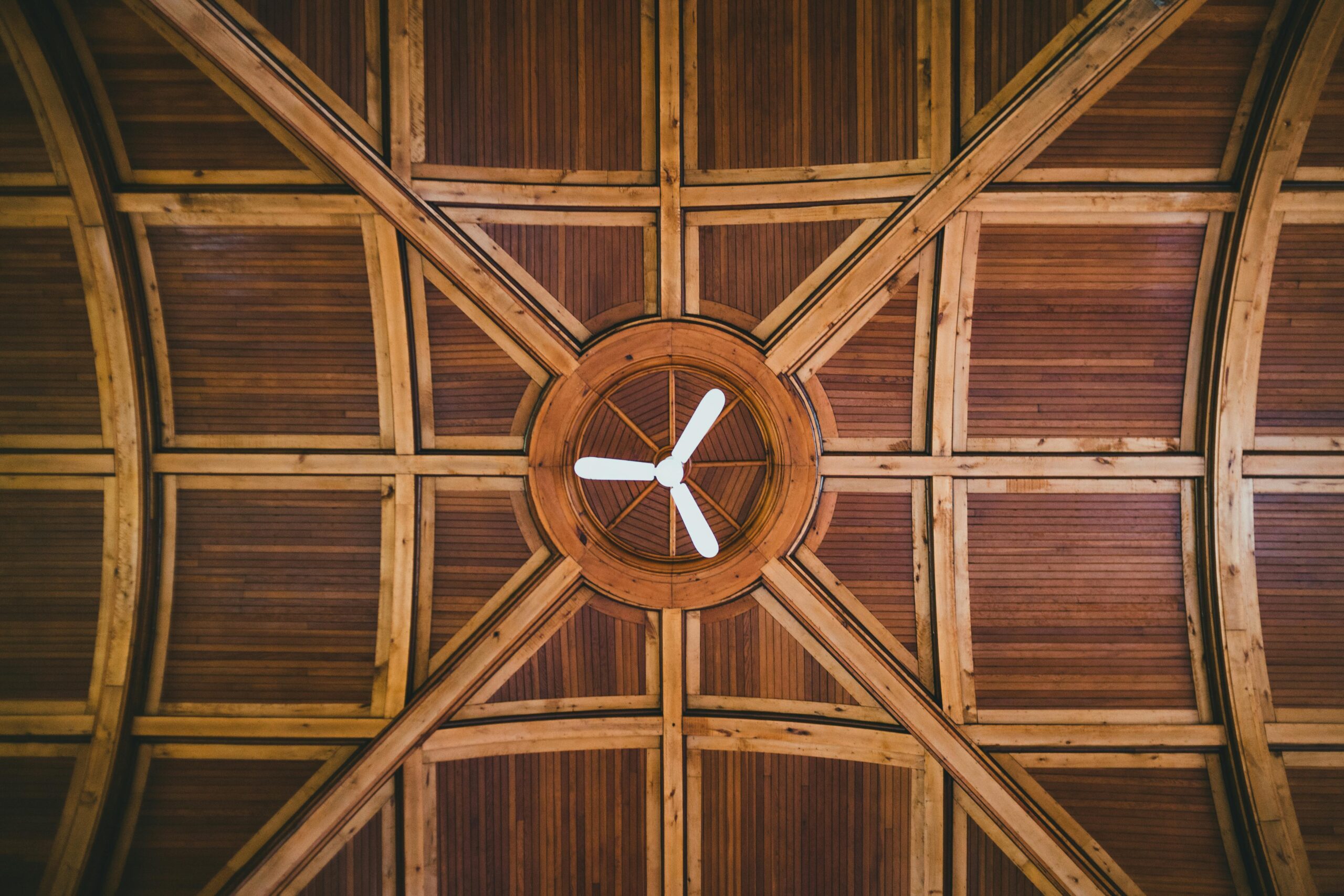 A symmetrical image of a wooden ceiling featuring a central fan with a starburst design.
