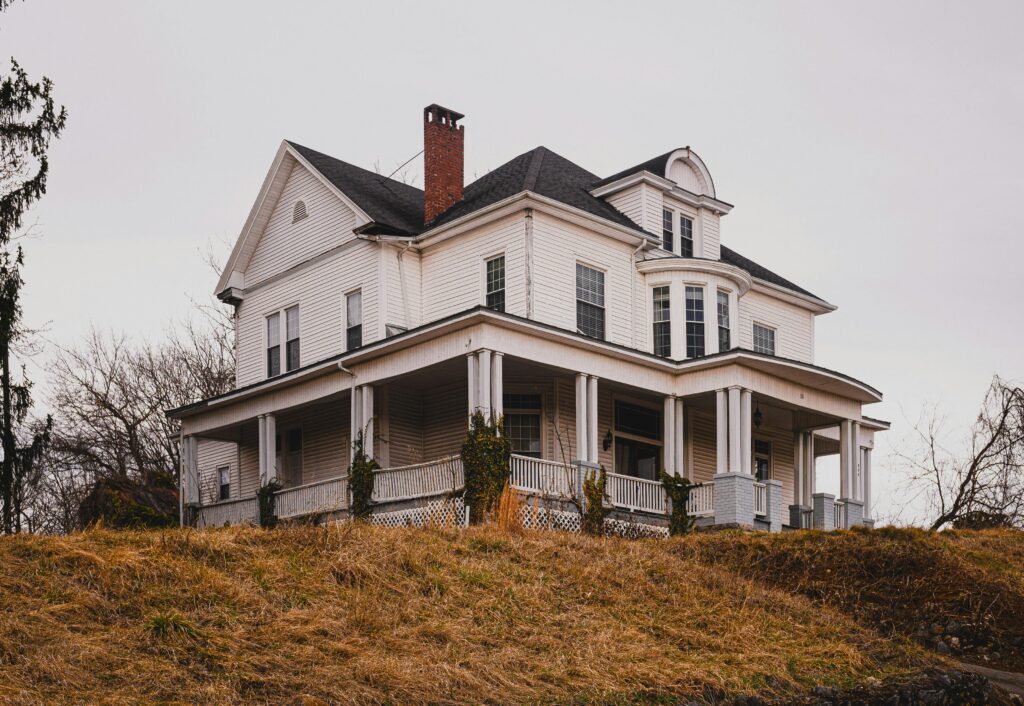 Beautiful historic white house with a wraparound porch set against autumn surroundings.