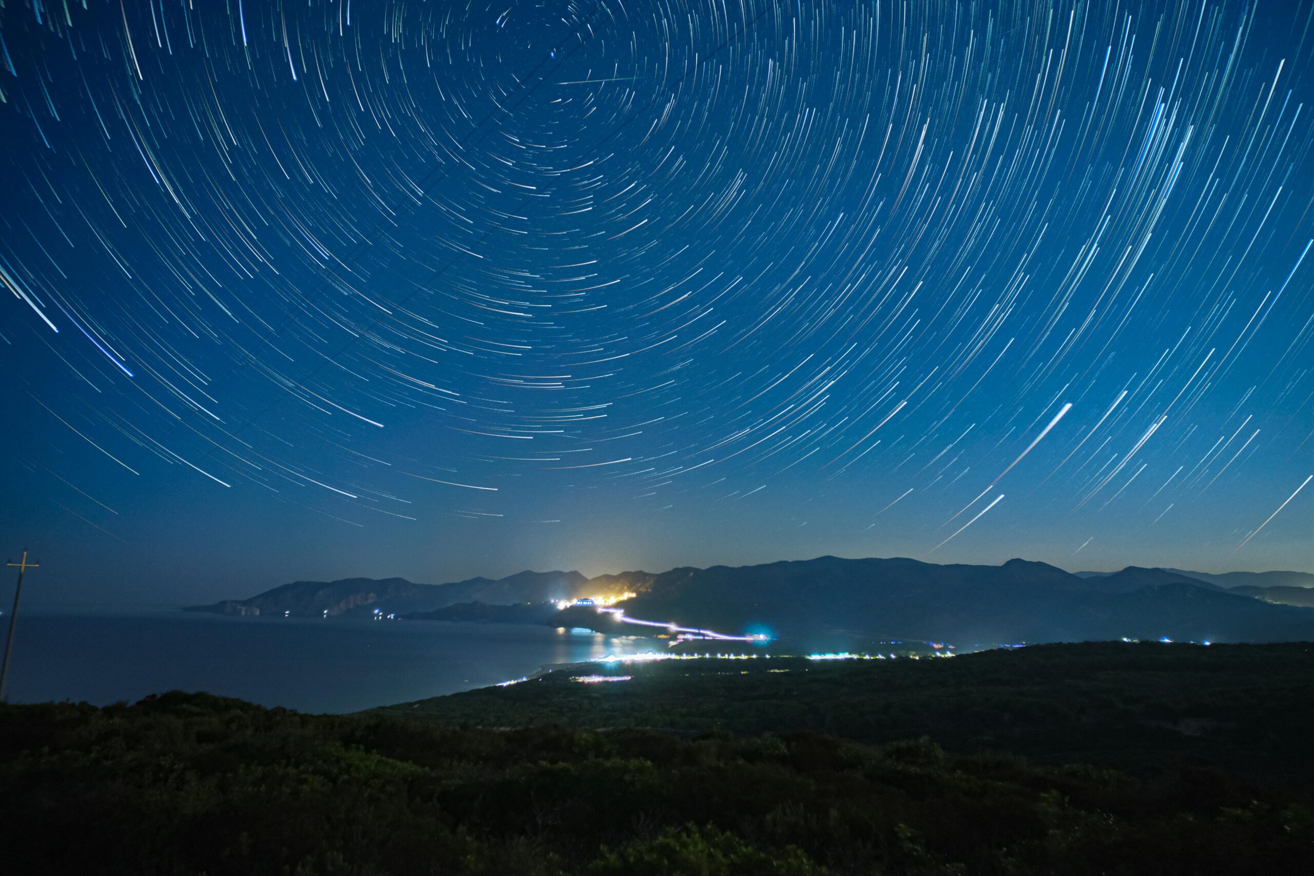 Long exposure of star trails over mountains and coastline at night in Sardinia, Italy.