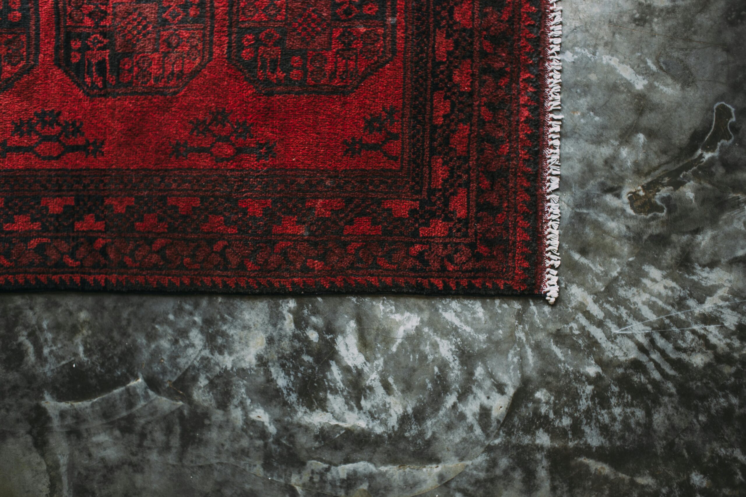 Close-up of a red floral patterned carpet on a textured concrete floor.