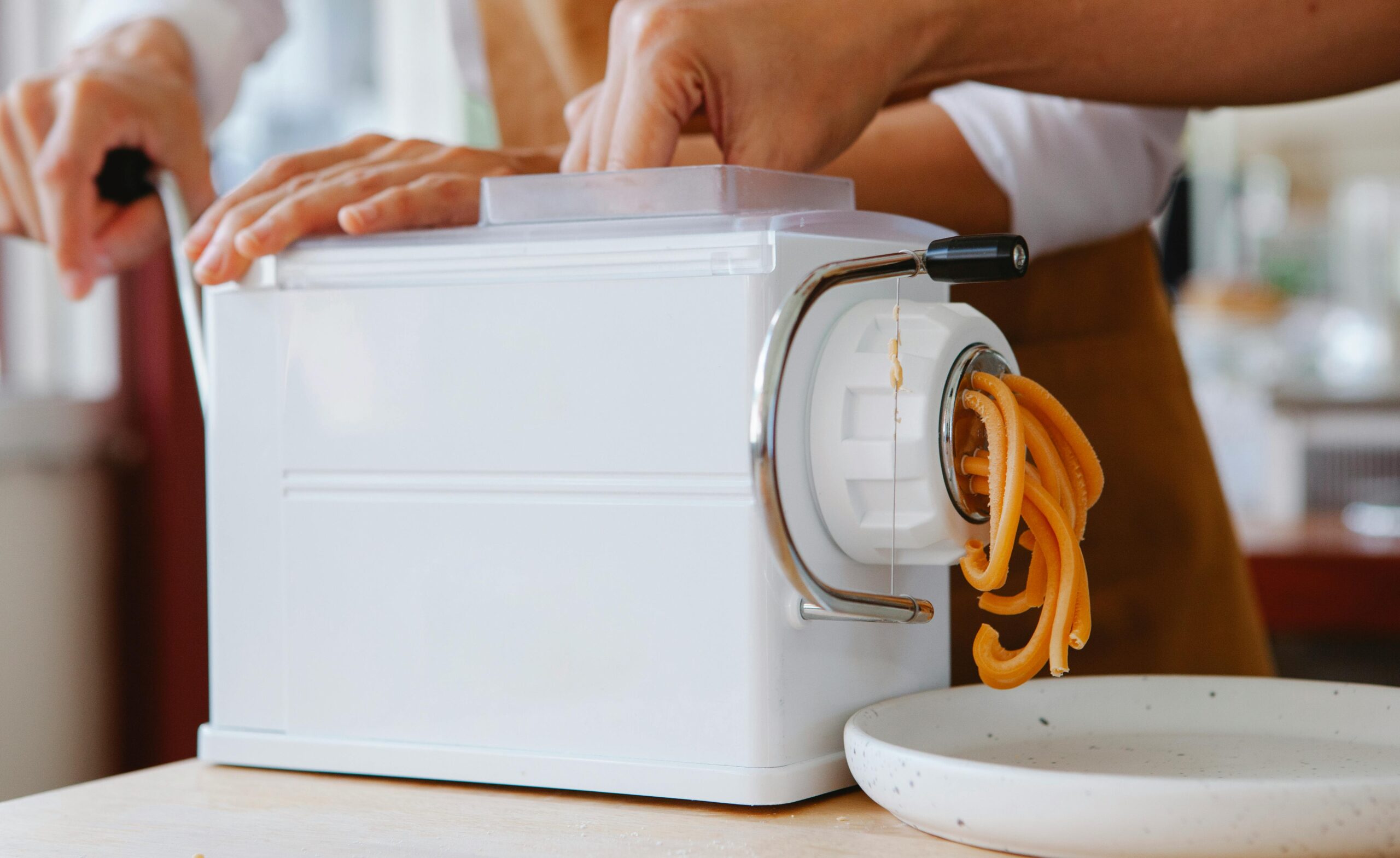Close-up of a pasta maker producing fresh noodles in a kitchen.