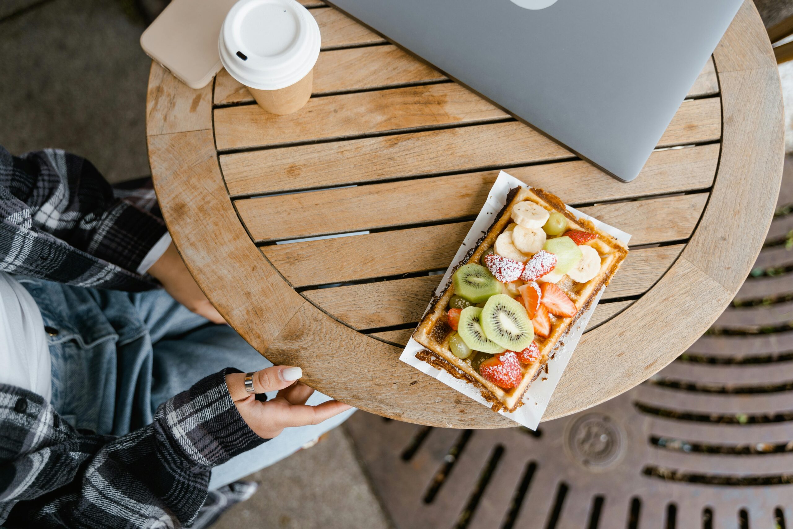 Delicious fruit-topped waffle on a wooden table with a coffee and laptop nearby.