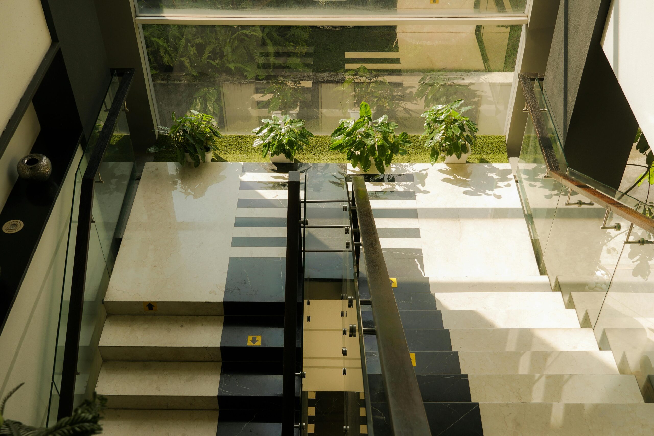 Sunlit modern staircase with large windows and decorative plants in Bandung, Indonesia.