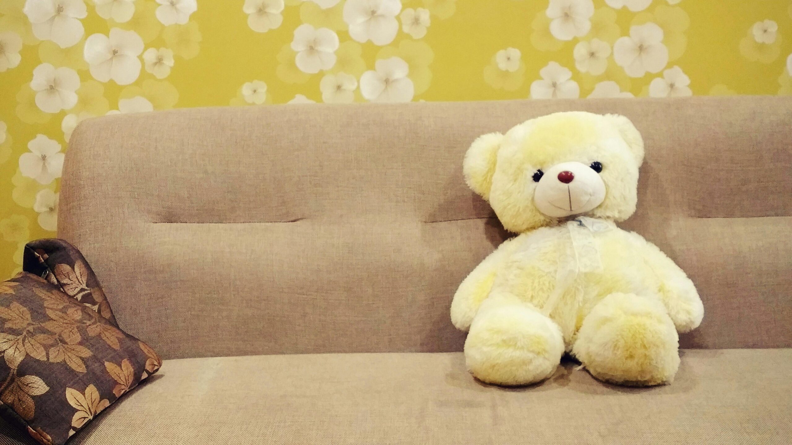 A cozy yellow teddy bear on a sofa with floral wallpaper, ideal for kids' room decor.